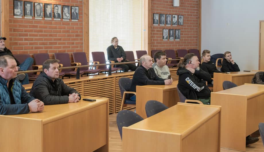 Kymmenen ihmistä istuu valtuustosalissa ja kuuntelevat keskittyneesti.